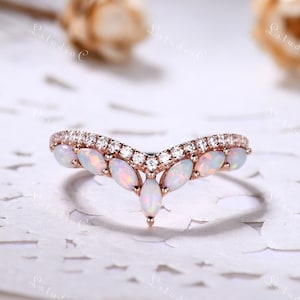 May include: A delicate rose gold ring with a V-shaped band adorned with a row of sparkling white gemstones and a cluster of opal stones in the center.