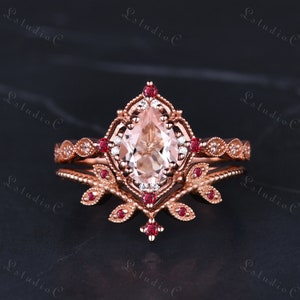 May include: A pear-shaped morganite engagement ring set in rose gold with a delicate floral design and small red gemstones. The ring is accented with smaller diamonds.