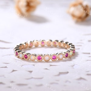 May include: A delicate gold band ring with alternating pink and white gemstones. The ring is set with small, round stones in a bezel setting.