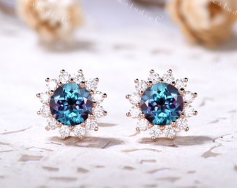 May include: A pair of stud earrings featuring a round, colour-changing alexandrite centre stone surrounded by a halo of small, clear, round-cut white stones set in a rose gold metal frame, creating a floral-inspired design.