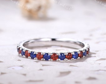 May include: A silver band ring with a row of alternating red and blue gemstones.
