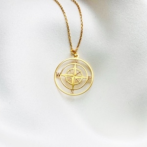 Pu&ograve; includere: Una collana con ciondolo a forma di bussola in oro. Il ciondolo della bussola presenta un design dettagliato con una stella al centro e le lettere N, S, E e W attorno al bordo.