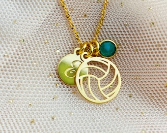 Può includere: Collana d'oro con un ciondolo a forma di pallavolo, un piccolo ciondolo con un'iniziale e una pietra preziosa verde.