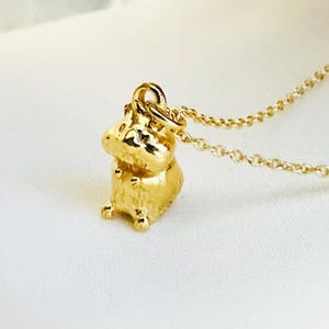 May include: A gold-coloured necklace with a small, detailed hamster charm. The hamster is sitting upright with its paws together.