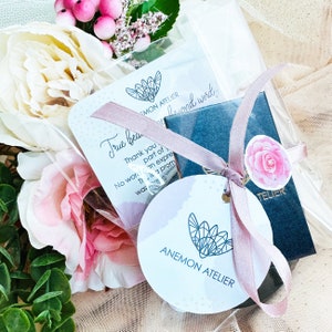 Puede incluir: Una peque&ntilde;a caja de regalo envuelta en una cinta rosa con una etiqueta blanca que dice "True beauty" y "Thank you for being part of... This is a promise... No words can express... was more... beyond words". La caja est&aacute; rodeada de flores rosas y una bolsa de pl&aacute;stico transparente.