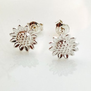 Puede incluir: Un par de pendientes de plata con forma de girasol. Los pendientes son pequeños y delicados, con un diseño sencillo.