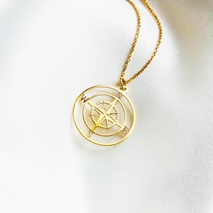 Pu&ograve; includere: Una collana d'oro con un ciondolo a forma di bussola. La bussola presenta un design dettagliato con le lettere N, S, E e W.