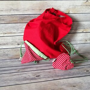 Könnte beinhalten: Zwei rote Stofftaschen mit weißen Punkten. Die größere Tasche ist eine Tragetasche mit Kordelzug. Die kleinere Tasche ist eine herzförmige Tasche mit Kordelzug.