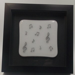 May include: A framed piece of art featuring a white background with gray musical notes and treble clefs. The frame is black.
