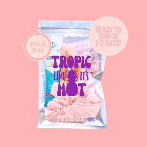 May include: A clear plastic bag with a pink scrunchie, a purple and white "Tropic Like It's Hot" design, and a small bottle of lotion. The bag has a white label that says "Ready to Ship in 1-2 Days!"