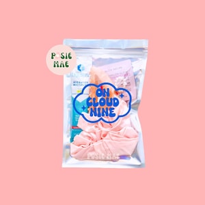 May include: A clear plastic bag with a pink scrunchie, a small bottle of hand sanitizer, and a card with the text "On Cloud Nine" in blue lettering. The bag has a sticker with the text "Posie Mae" in green lettering.