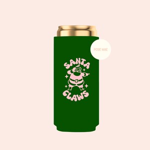 May include: A dark green slim can cooler featuring a light pink graphic of Santa Claus and the text "SANTA CLAWS" with small star accents. A small circular white tag with the text "POSIE MAE" is attached to the upper right side of the cooler.