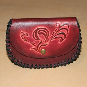 May include: A red leather coin purse with a black stitched edge and a floral design embossed on the front.