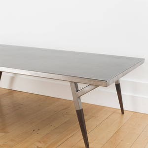 May include: A long, rectangular, silver coffee table with a simple, modern design. The table has a metal frame and wooden legs.