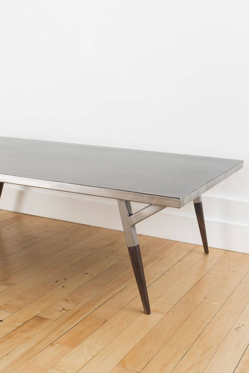 May include: A long, rectangular, silver coffee table with a simple, modern design. The table has a metal frame and wooden legs.