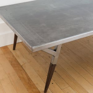 May include: A metal coffee table with a gray top and a silver metal frame. The table has four legs, two of which are made of dark wood.