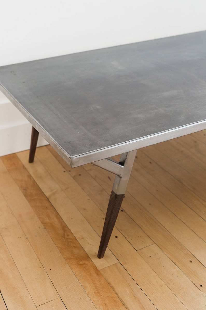 May include: A metal coffee table with a gray top and a silver metal frame. The table has four legs, two of which are made of dark wood.