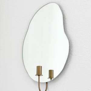 Side angle of the wall mounted organic shape Mar Mirror Candle Sconce or Mirror Candle Holder. The candleholder is gold & not holding a candle. The reflection is of the gold candle holder and white background.