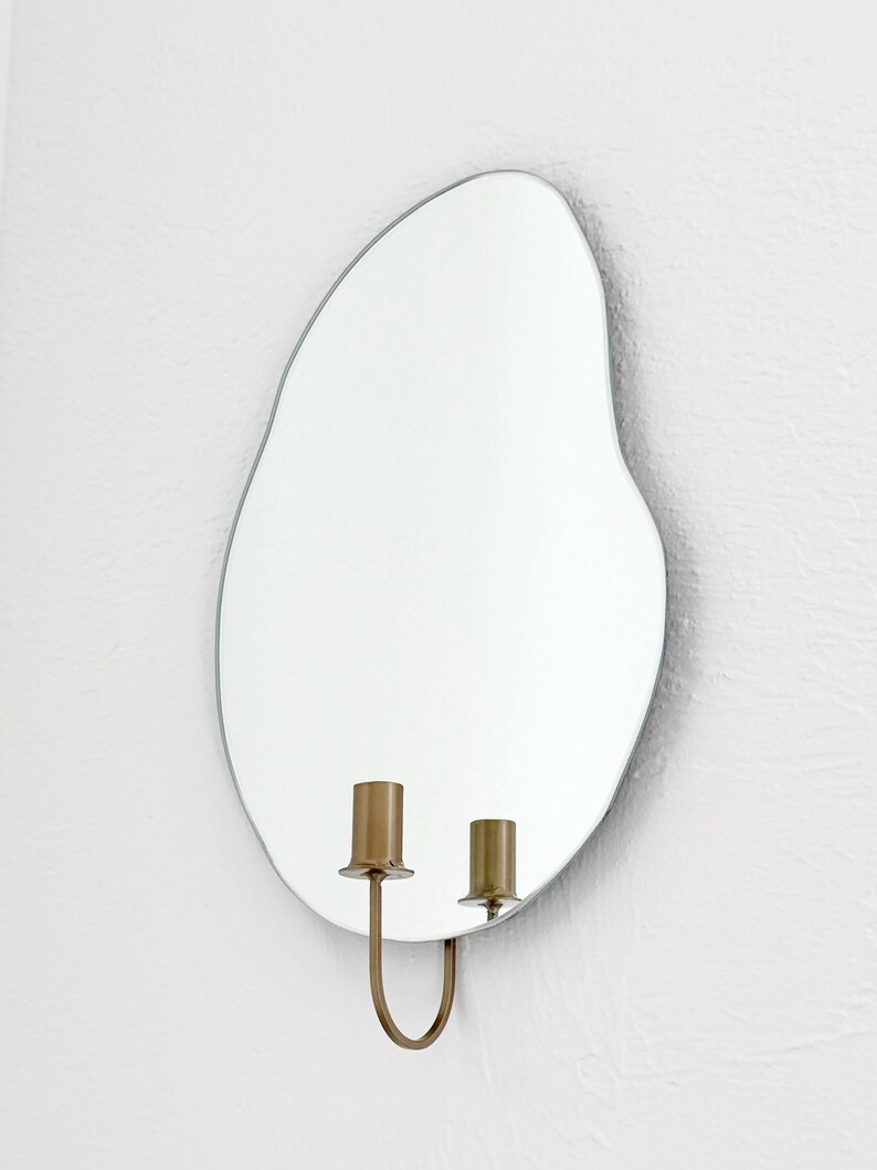 Side angle of the wall mounted organic shape Mar Mirror Candle Sconce or Mirror Candle Holder. The candleholder is gold & not holding a candle. The reflection is of the gold candle holder and white background.