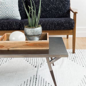 May include: A metal coffee table with a wooden tray on top. The tray holds a white decorative sphere and a potted succulent plant. The table is on a white and black striped rug.