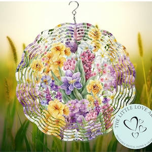 May include: A colourful floral design metal wind spinner with a gold and white background. The wind spinner features a variety of flowers, including purple, yellow, and white. The wind spinner is hanging from a hook and is surrounded by green grass.