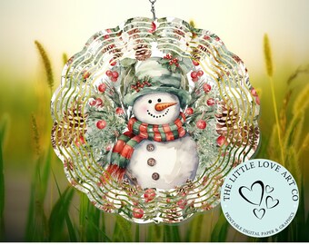 Op de afbeelding: Een aquarel-achtige sneeuwpop met een groene hoed en een rood-groene sjaal, omringd door dennenappels, hulstbesjes en groen. Het ontwerp is op een metalen windmolen met een gouden achtergrond. De tekst "The Little Love Art Co. Printable Digital Paper & Graphics" staat op een blauwe cirkel.