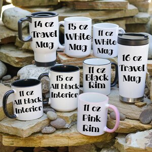May include: A collection of seven white ceramic mugs with black accents. The mugs are in various sizes, ranging from 11 to 16 ounces. The mugs feature different designs, including a travel mug, a mug with a black rim, and a mug with a pink rim. The mugs are displayed on a background of brown rocks.