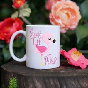 May include: White ceramic mug with a pink flamingo illustration and the text "Stand Tall Be Proud".