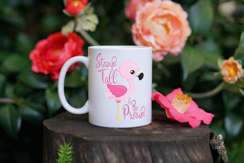 May include: White ceramic mug with a pink flamingo illustration and the text "Stand Tall Be Proud".