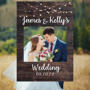 May include: Rustic wooden photo booth frame with string lights, a photo cutout, and the text "James & Kelly's Wedding 08.10.19".