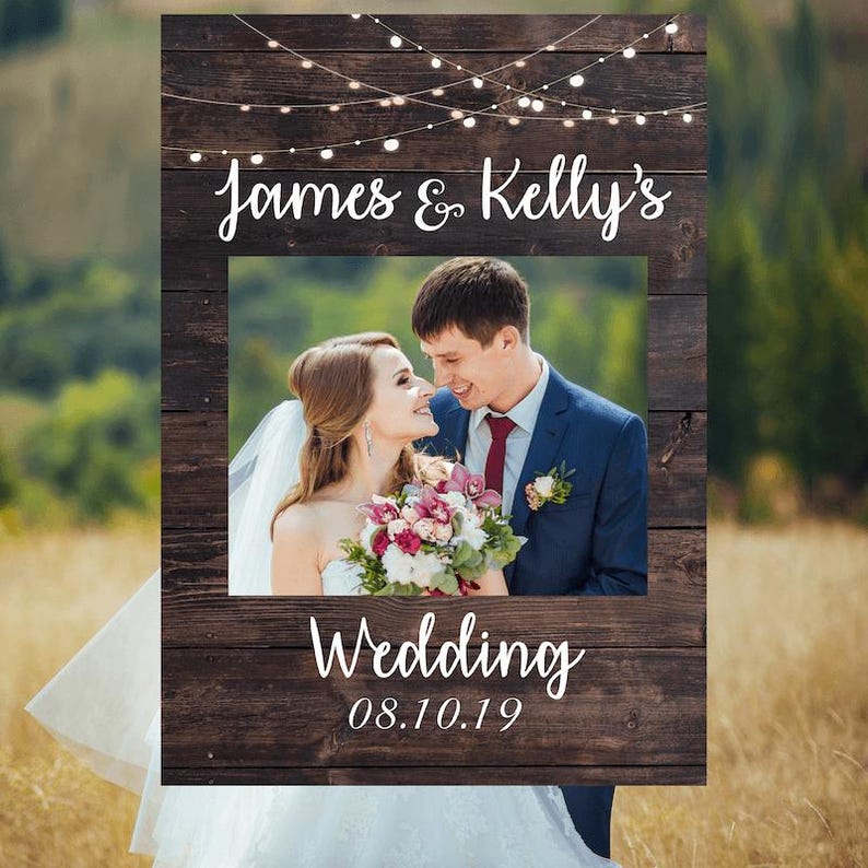 May include: Rustic wooden photo booth frame with string lights, a photo cutout, and the text "James & Kelly's Wedding 08.10.19".