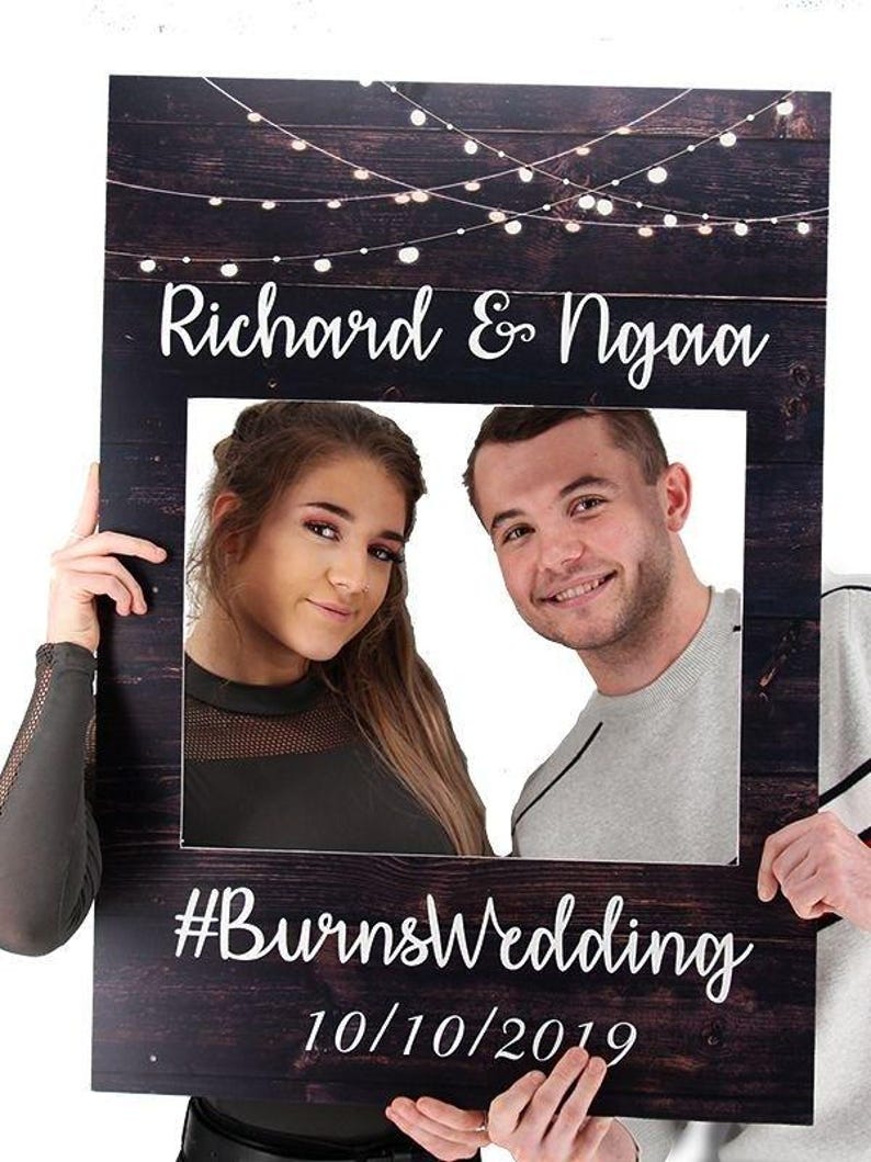May include: A rustic wooden photo booth prop with string lights, a white frame, and the text "Richard & Ngaoa #BurnsWedding 10/10/2019".