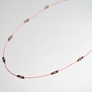 May include: A delicate pink string necklace with small blue and gold beads.
