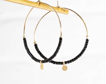 May include: Gold hoop earrings with black beads and a small gold charm.