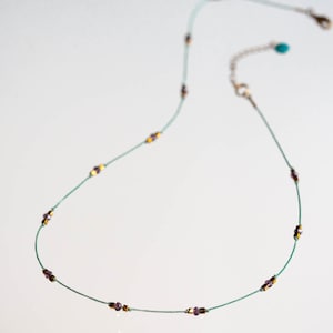 May include: A delicate green necklace with small purple and gold beads.
