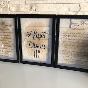 May include: Three framed prints with black frames. The center print has a white background with the text "Afiyet Olsun" in black lettering and a set of three black cutlery silhouettes. The left print has a white background with Arabic text and the text "Bereket Duasi" in black lettering. The right print has a white background with Arabic text and the text "Karınca Duasi" in black lettering.