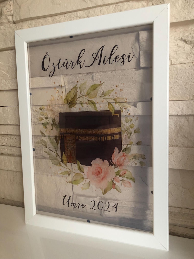 Puede incluir: Una impresi&oacute;n enmarcada en blanco con una ilustraci&oacute;n de acuarela de la Kaaba, un dise&ntilde;o floral y el texto "&Ouml;zt&uuml;rk Ailesi Umre 2024".