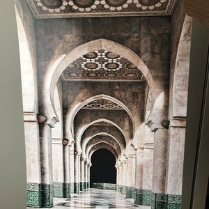 May include: A long hallway with a series of arches and columns. The floor is tiled in black and white, and the walls are a light beige. The arches are decorated with intricate patterns, and the ceiling is adorned with a repeating pattern of circles.