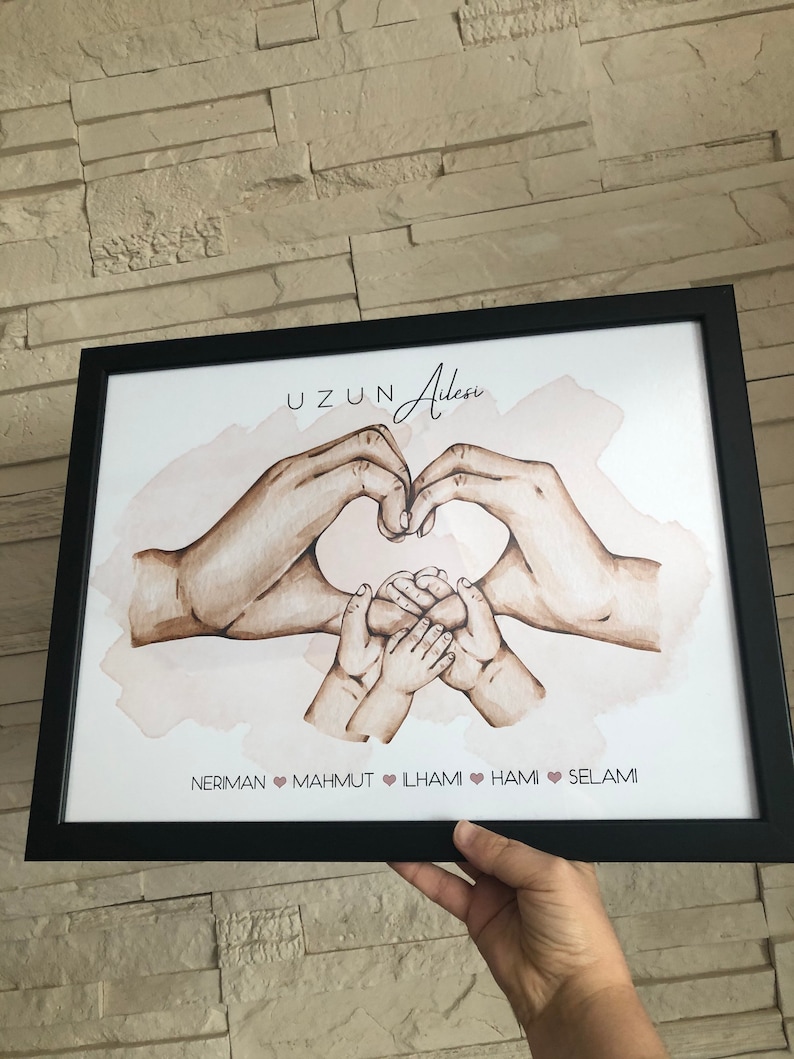 May include: A framed print with a watercolor illustration of two hands forming a heart shape around three smaller hands. The print has the text "UZUN Ailesi" at the top and the names "NERIMAN, MAHMUT, LHAMI, HAMI, SELAMI" at the bottom.