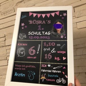 Puede incluir: Una pizarra negra con marco blanco, decorada con estrellas, banderas y corazones rosas y blancos. La pizarra tiene el texto "B&Uuml;ŞRA'S 1. SCHULTAG 15.09.2023" y una foto de una ni&ntilde;a. Tambi&eacute;n incluye el texto "ICH BIN 6! Jahre alt 1,10 m gro&szlig; & wiege 16 kg." y "Wenn ich gro&szlig; bin, werde ich &Auml;rztin."  La pizarra tambi&eacute;n incluye el texto "ICH... Fahrrad fahren basteln tanzen".