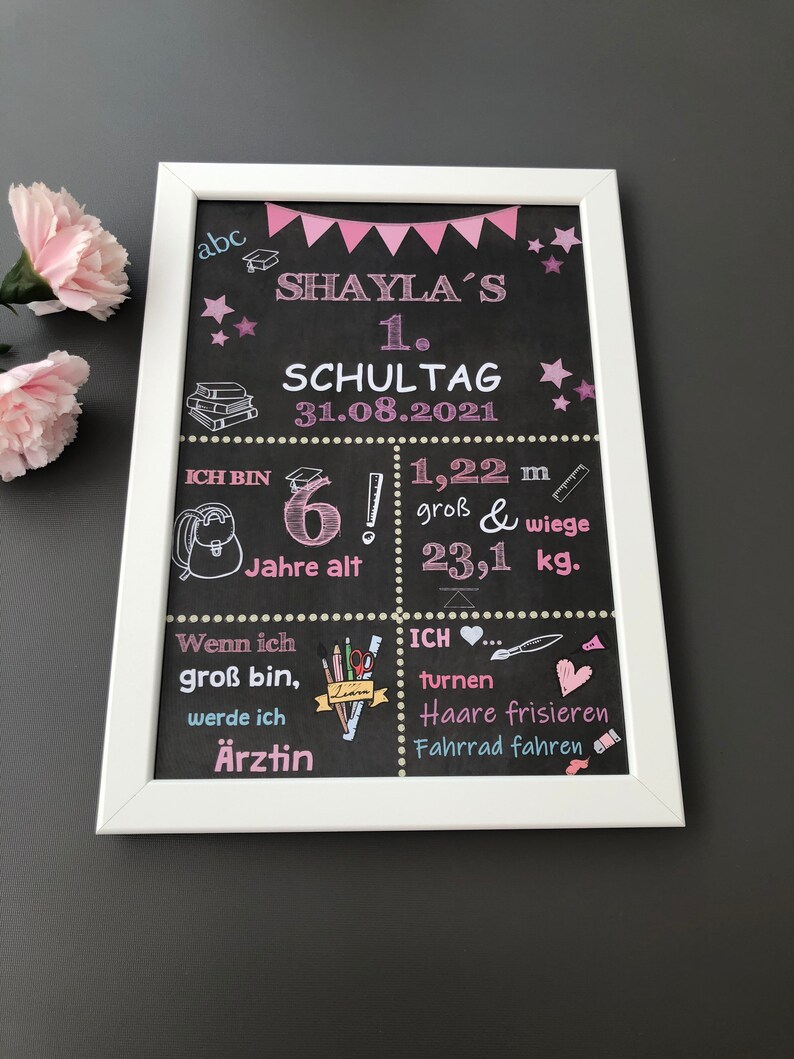 Puede incluir: Una pizarra negra con marco blanco, decorada con detalles en rosa y azul. La pizarra dice "Shaylas 1. Schultag 31.08.2021" e incluye detalles sobre la edad, la altura y el peso del ni&ntilde;o. Tambi&eacute;n enumera las actividades que le gustan al ni&ntilde;o, como hacer gimnasia, peinarse y andar en bicicleta.