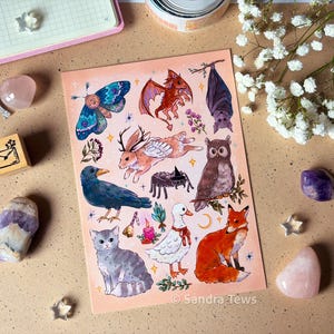 Peut inclure: Une impression d'art rectangulaire présentant une collection d'illustrations à l'aquarelle incluant un papillon de nuit, un petit dragon rouge, une chauve-souris, un jackalope, une araignée, un hibou, un corbeau, un chat, un canard et un renard.