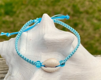 Puede incluir: Un brazalete trenzado azul claro con un dije de concha blanca y cuentas de vidrio azules.