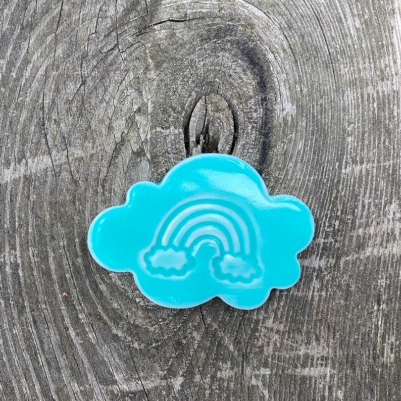 Op de afbeelding: Een turquoise blauwe wolkvormige koekjesuitsteker met een wit regenboog- en wolkenontwerp.