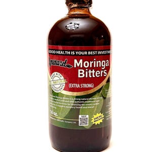 May include: A dark brown bottle of Amenazel Moringa Bitters with a black cap. The label features the text "Moringa Bitters" and "Extra Strong" on a red background. The bottle contains 16 oz of liquid.