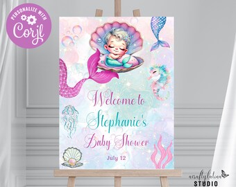 May include: A welcome sign for a baby shower with a mermaid theme. The sign features a pink and purple mermaid tail, a baby mermaid sleeping in a seashell, and the text "Welcome to Stephanie's Baby Shower July 12".