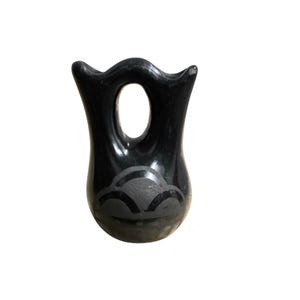 May include: A black, handcrafted vase with a unique, open-handled design. The vase features a decorative, etched cloud-like pattern near the base. The vase has a glossy finish and a distinctive, organic shape.