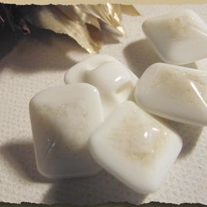 Op de afbeelding: Vijf witte glazen knopen met een subtiele glans. De knopen zijn in verschillende vormen en maten, sommige hebben een gat in het midden.