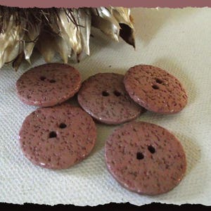 May include: Five brown speckled buttons with two holes each. The buttons are arranged in a semi-circle on a white surface.
