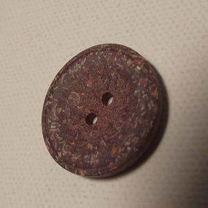 May include: A close-up of a round, dark brown button with two holes. The button has a textured surface with lighter brown and tan speckles. Suitable for sewing projects and crafts.
